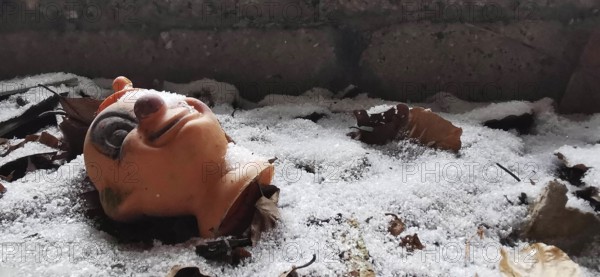 Worn doll's head lies in the snow between autumn leaves