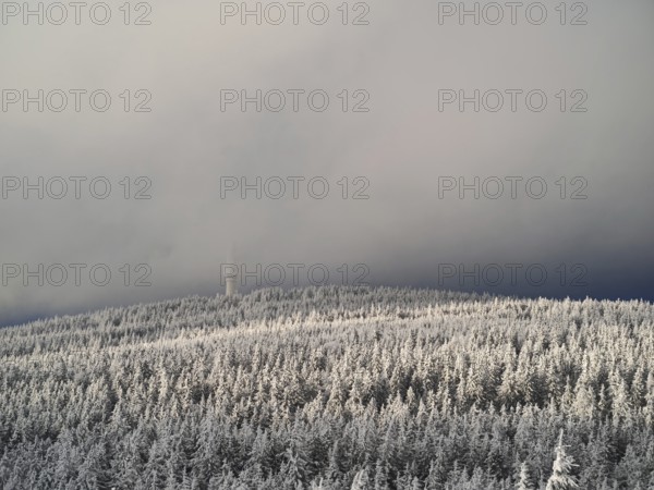 A snow-covered forest with a tower disappearing in fog on a hill, view from Nusshardt towards Bacöfele on the Schneeberg, Fichtelgebirge, Bavaria