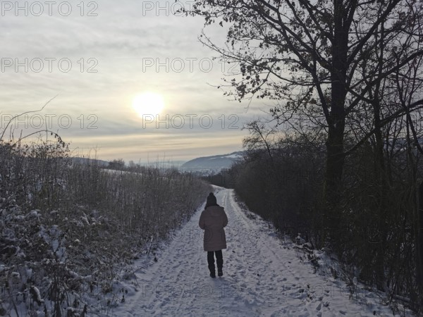 Woman walking on a snowy path at sunset through the winter landscape, Franconian Forest