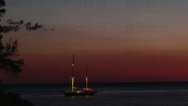 Sailing boat on still sea at sunset, illuminated by dwindling daylight