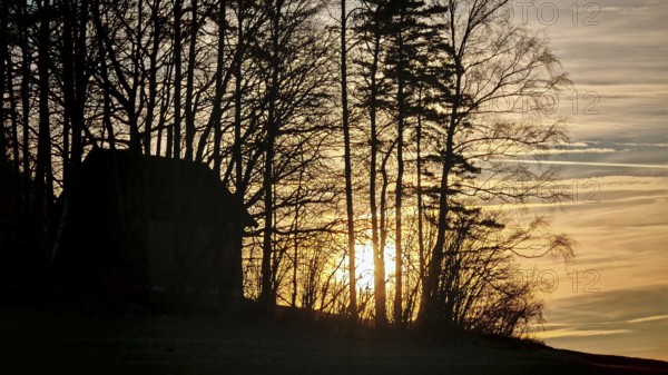 Barn and tree silhouettes against rising sun and colorful sky at dawn