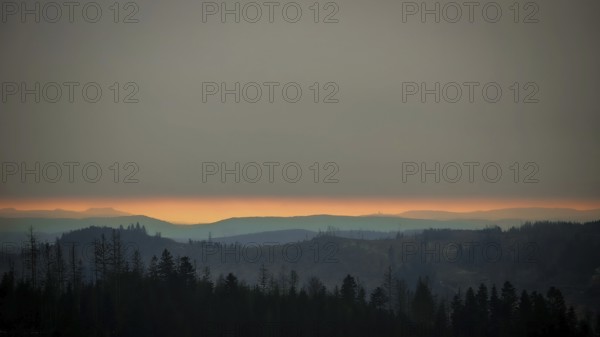 Twilight landscape with looming hills and trees under a cloudy sky