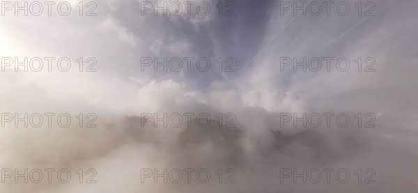 Soft cloud formations over foggy mountain peaks in mild light