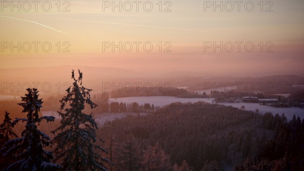 Colourful sunset over a snowy hill and forest landscape