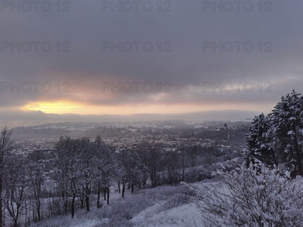 Snow-covered hills and trees under a dramatic sunset, view over Kronach in the Franconian Forest
