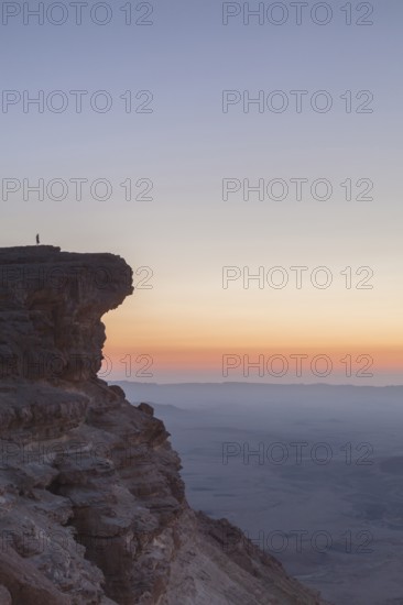 Mitzpe Ramon, Israel, Negev Desert, A woman in the vast overlooking the vast Makhtesh Ramon crater at sunset from a cliff part of the Ramon Nature Reserve