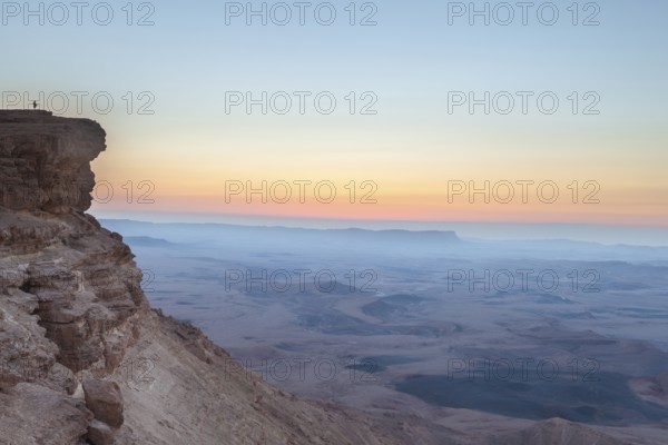Mitzpe Ramon, Israel, Negev Desert, A woman in the vast overlooking the vast Makhtesh Ramon crater at sunset from a cliff part of the Ramon Nature Reserve