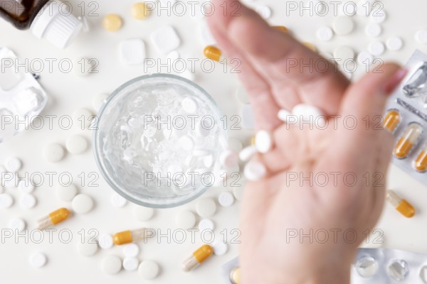 Hand pouring white tablets into a glass with water on a light background