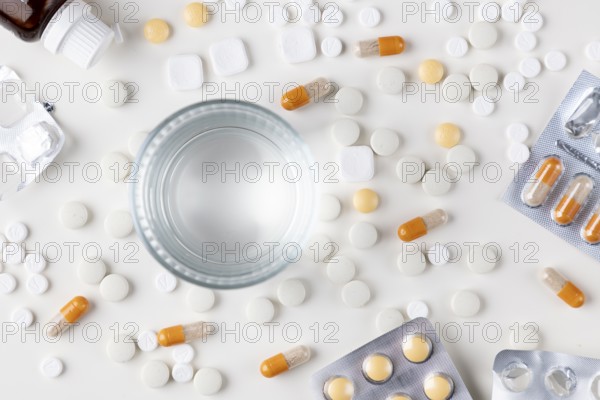 Table with scattered tablets, blister packs and a glass of water