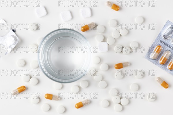 Glass of water with tablets and orange-white capsules on a white background