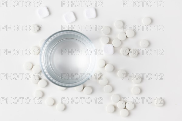 Glass of water with lots of scattered white tablets on a white surface
