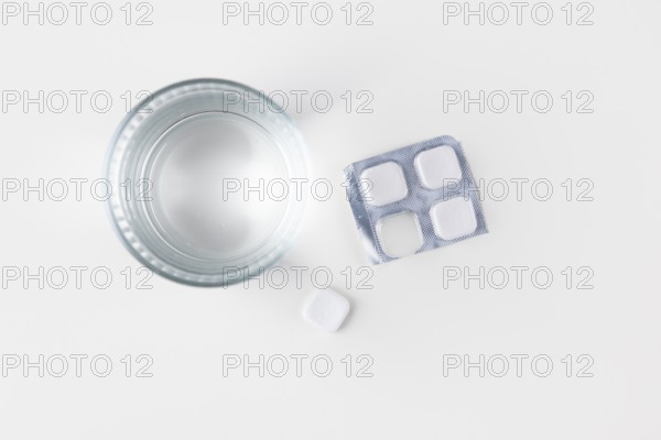 Glass of water with packaging and tablets on a white surface