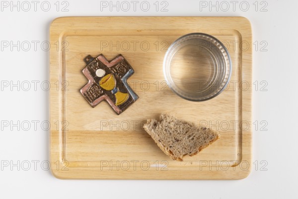 Wooden board with a cross, a glass of water and a piece of bread