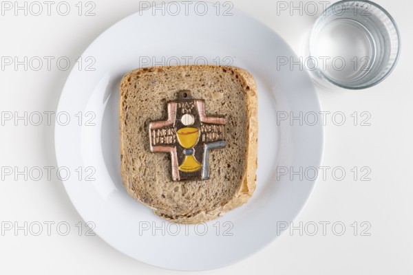 A slice of bread with a cross symbol on it, water next to it, fasting