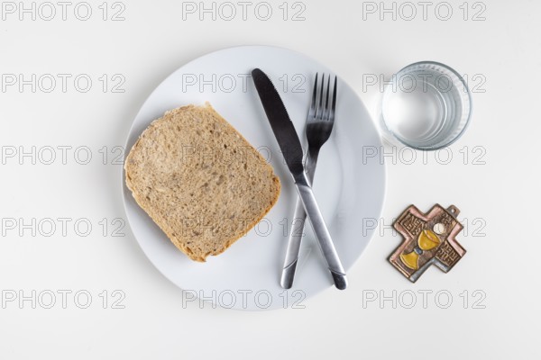 A plate with a slice of bread, cutlery, water glass and cross, Lent