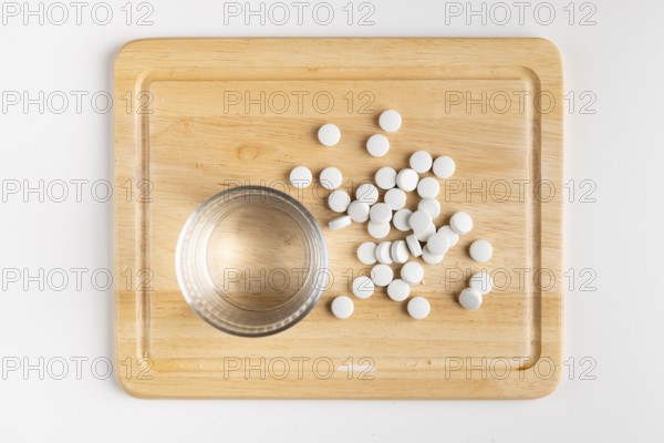 Wooden board with glass of water and scattered tablets