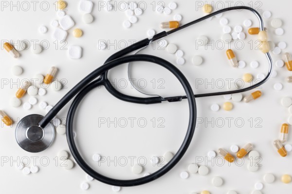 Stethoscope lies on a white surface surrounded by tablets and capsules