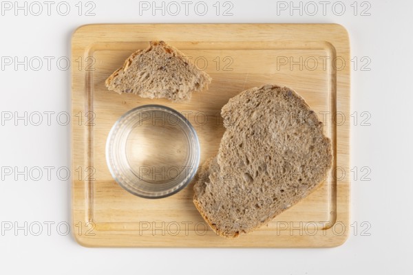Wooden board with a large and a small piece of bread and a glass of water