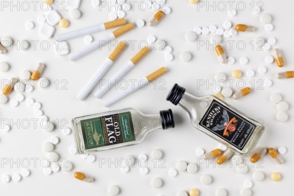 Two small alcohol bottles next to tablets, capsules and cigarettes on a white background