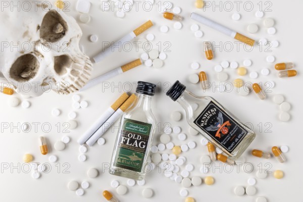 Skulls and alcohol bottles surrounded by tablets, capsules and cigarettes on a white background
