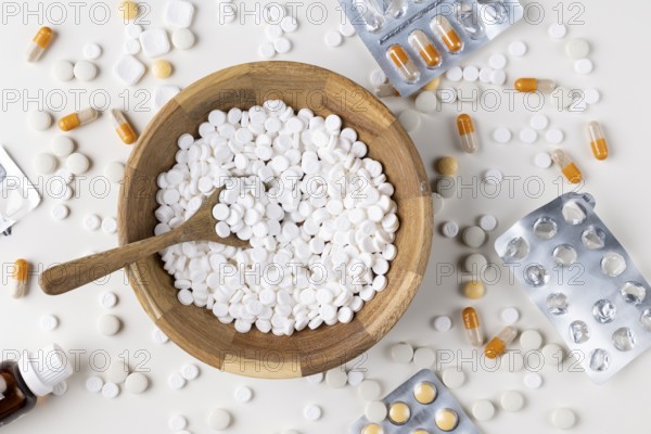 Wooden bowl full of tablets with a spoon and scattered blister packs