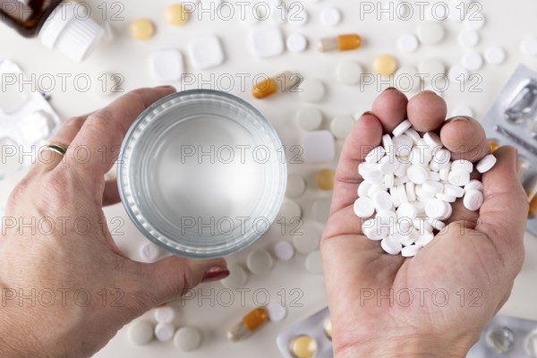 Two hands hold a glass of water and a handful of tablets across a table