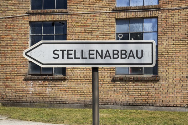 (photo montage) Directional arrows with the inscription JOB REDUCTION in front of an old industrial building