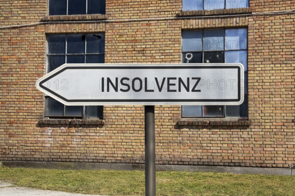 (Photo montage) Directional arrows with the inscription BANKRUPTCY in front of an old industrial building