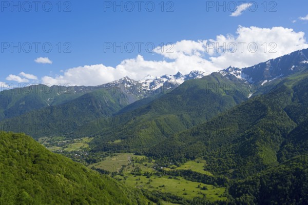 Green valley with densely wooded slopes and distant mountains under blue sky with clouds, landscape near Iskari, Mingrelia and Upper Svaneti, Samegrelo-Zemo Svaneti, Svaneti, High or Greater Caucasus, Georgia