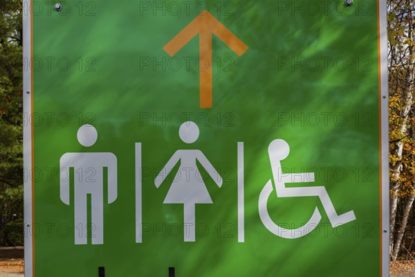 White painted outlines of adult male, female and person in wheelchair on green pictogram sign posted outdoors pointing the way to public restrooms, Quebec, Canada