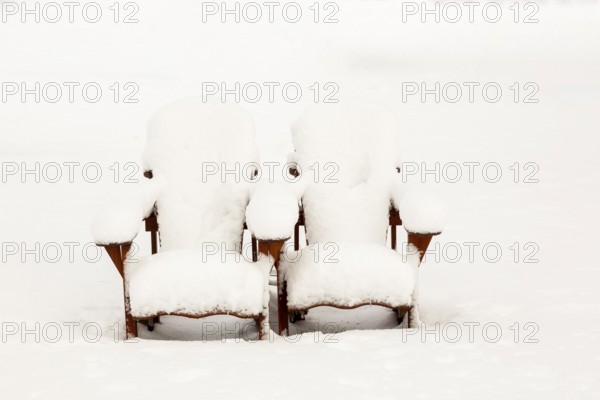 Two brown stained wooden Adirondack chairs covered in freshly fallen winter like snow in public park in late autumn, Quebec, Canada