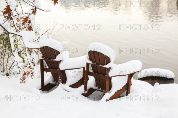 Two brown stained wooden Adirondack chairs by riverside covered with winter like snow in late autumn, Ile des Moulins, Old Terrebonne, Quebec, Canada