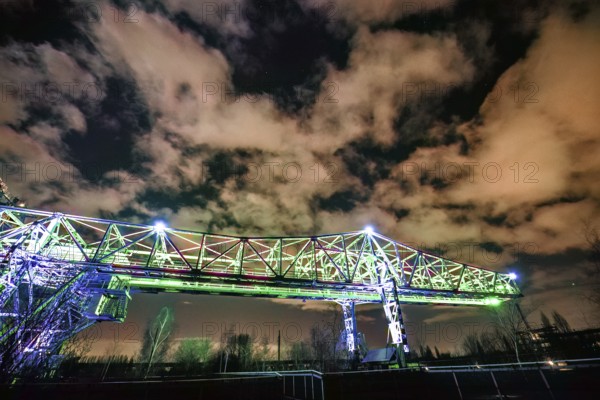 Illuminated bridge at night under a dramatically cloudy sky with green light, Landschaftspark Duisburg Nord, Duisburg, North Rhine-Westphalia, Germany