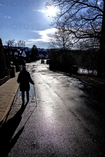 Aetere woman with sticks running on rain-wet road, back light, Eckental, Middle Franconia, Bavaria, Germany