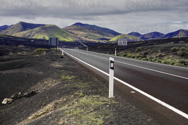 Empty road leads through a volcanic mountain landscape under cloudy sky, Yaiza Lanzarote