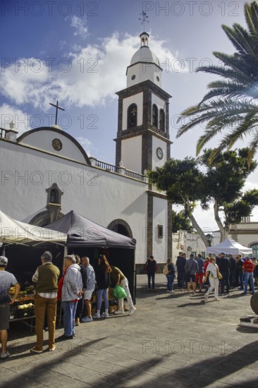 Church front with market scene, people gather around tents on a sunny square, Arrecife Lanzarote