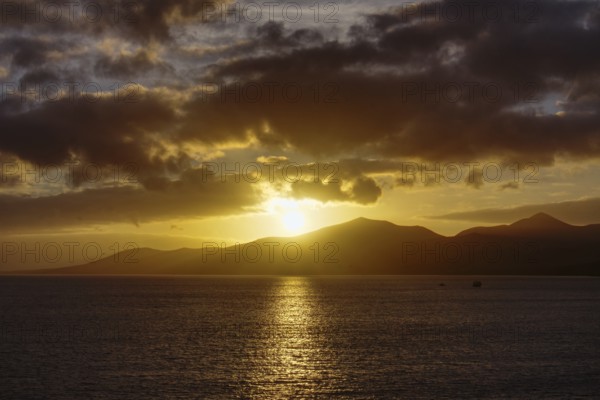 Sunset over the sea with golden reflections on the water surface, mountains on the horizon, Puerto del Carmen Lanzarote