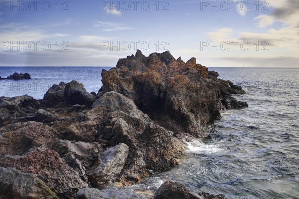 Rough rock formation jutting into the sea surrounded by waves under a slightly cloudy sky, Puerto del Carmen Lanzarote