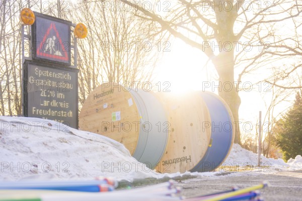 Sun rays fall on cable rolls next to a construction site sign surrounded by snow, fibreglass groundbreaking, Freudenstadt, Germany