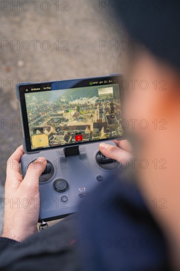 Person controls a drone with a remote control whose screen shows a city, fiberglass groundbreaking, Freudenstadt, Germany