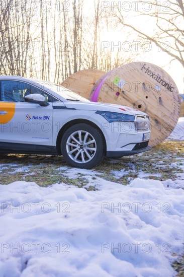 A car stands next to large rolls of cable on a snow-covered meadow in winter, fibreglass groundbreaking, Freudenstadt, Germany