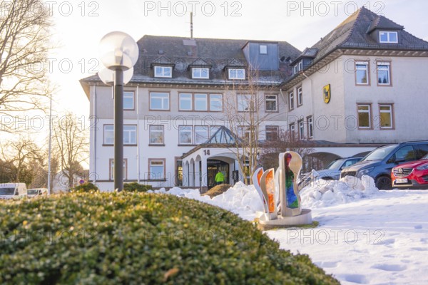 A snowy building with sculptures and parked cars in winter light, fibreglass groundbreaking, Freudenstadt, Germany