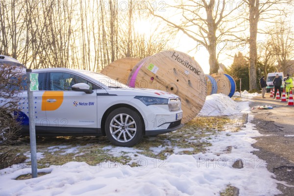 A car is parked next to large cable drums in a wintry environment with construction work, fibreglass groundbreaking, Freudenstadt, Germany