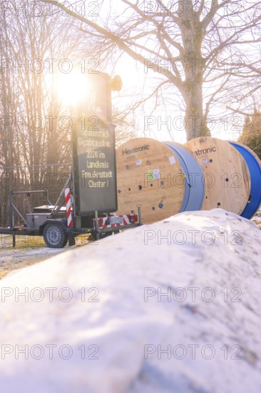Cable rolls and a construction site sign along a snowy road when the sun is low, fibreglass groundbreaking, Freudenstadt, Germany