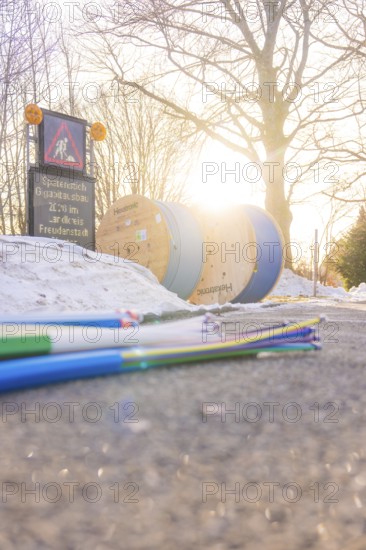 Colored cables in front of cable rolls in sunlight along a snowy road, fiberglass groundbreaking, Freudenstadt, Germany