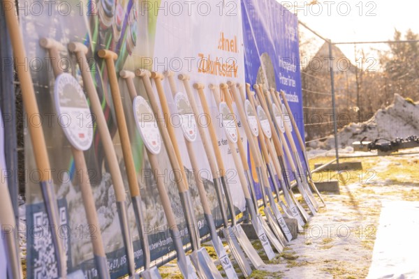 Several spades in front of colorful banners on a snow-covered building site in the winter sun, fiberglass groundbreaking, Freudenstadt, Germany