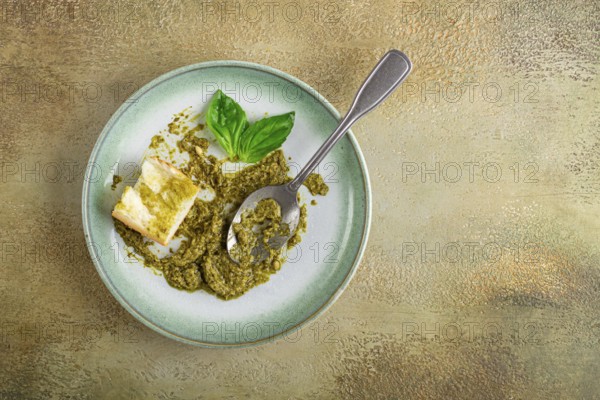 On a platter is a pesto sauce made from fresh basil, with a slice of bread and a spoon on a plate. The pesto sauce looks creamy and green, and the bread is partially eaten
