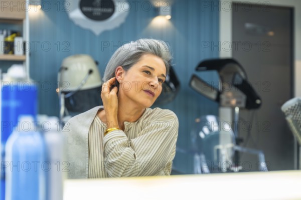 Senior woman with silver hair smiles, admiring her stylish short haircut in a salon mirror, feeling confident, refreshed and elegant after a professional haircut and pampering