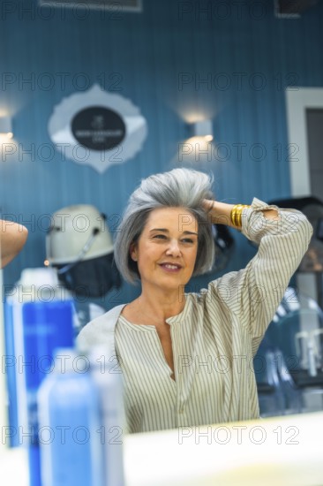 Mature woman looking at her reflection, touching her fresh gray hairstyle, and smiling in a modern beauty hair salon, feeling confident and happy with her new look