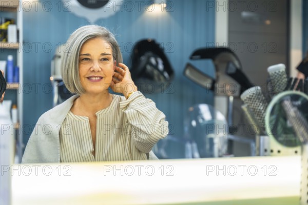 Senior woman looking at her reflection in the salon mirror, smiling and admiring her new short haircut and elegant grey hairstyle, representing beauty, self care, and confidence